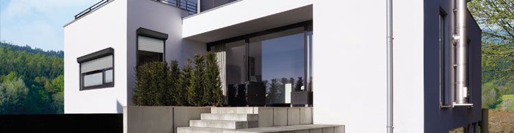 Modernes weißes Einfamilienhaus mit großen Fenstern, Terrasse, Treppe und grünen Büschen im Vordergrund.